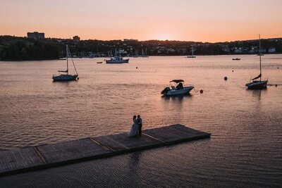 A bride and groom dance at the end of a dock in sunset. 