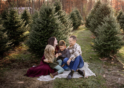 Family of 4 hugging in a christmas tree farm mini session