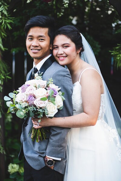 Groom in grey with bride holding a classic  bouquet  of purple and white roses
