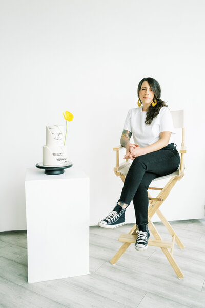 Owner - Johannah sitting next to a cake she made on a pedestal