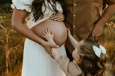 Toddler girl reaches up and touches her pregnant mother's belly.