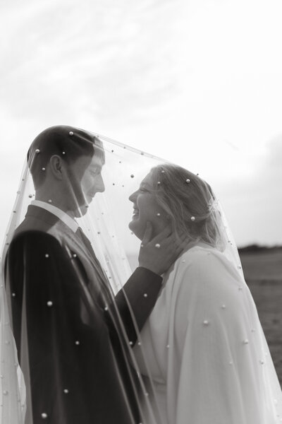 bride and groom under vail on wedding day black and white photo