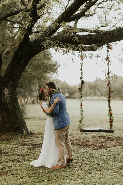 Bride and groom kissing by the romantic swing at Puakea Ranch during their luxury Hawaii wedding.