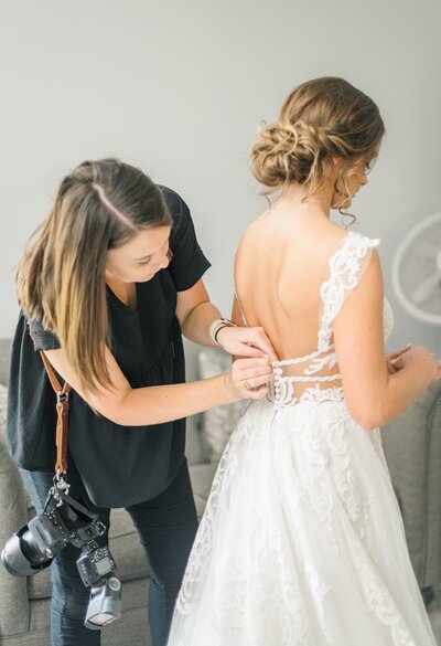 wedding photographer educator katiera helping a bride button up her dress before wedding ceremony