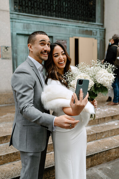 Bride and groom excited after walking out of their city hall ceremony, taking a selfie together. Bride has babys breath flower bouquet. - by Daniella Diaz Photo