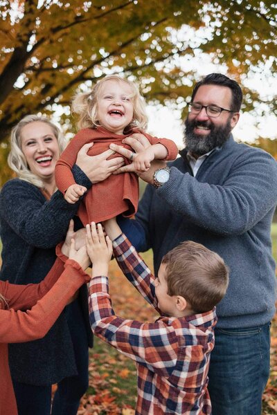 A joyful family lifting their toddler daughter during an autumn outdoor photography session in Cleveland, surrounded by vibrant fall leaves.