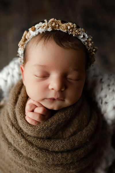 newborn baby girl wrapped in a brown swaddle with a floral crown sleeping during her york newborn session