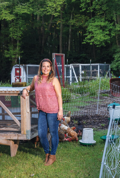 Talon posing in front of a chicken enclosure with her arm resting on a coop. 