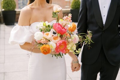 Bride and groom holding hands while the bride holds a colorful bouquet at a wedding at Boca Cincinnati