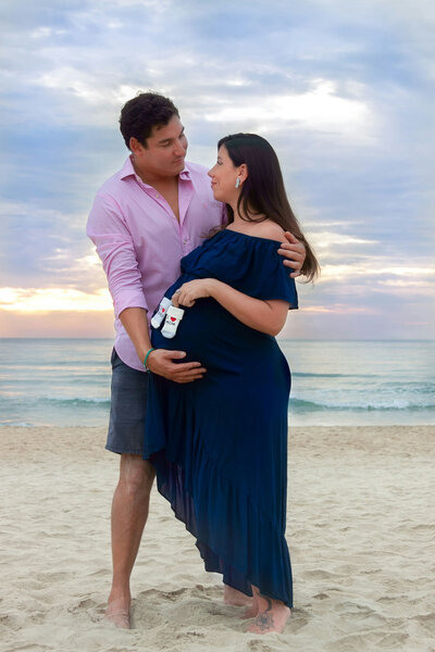 Man and pregnant woman are posing for a picture on the beach