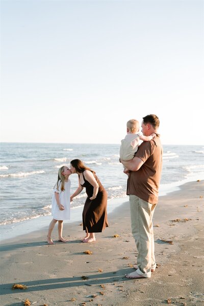 Family of mom and dad with young daughter walking outside with son swinging in the air holding parents hands