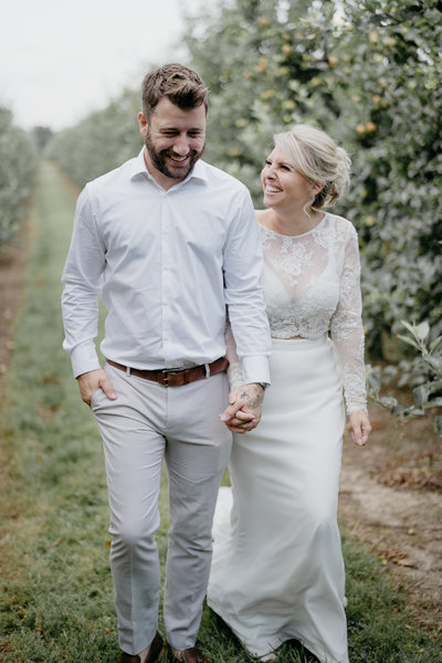 Natural photo of bride and groom laughing and joking as they walking in an orchard at The Barnyard wedding venue, Sittingbourne, Kent, UK