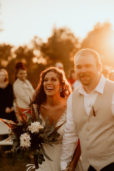 bride and groom holding hands and exiting from their wedding ceremony as the sun sets behind them at their Little Rock outdoor wedding venue