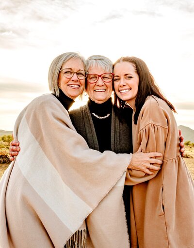 3 generations of mothers smiling cheek to cheek and hugging on a cloudy day in Phoenix. Captured by Cactus & Pine Photography