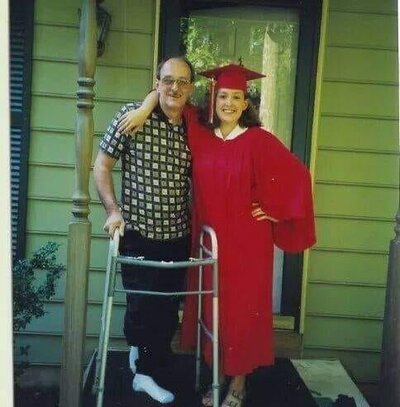 Kara Michelle standing with her stepfather in her graduation gown, smiling on a porch.