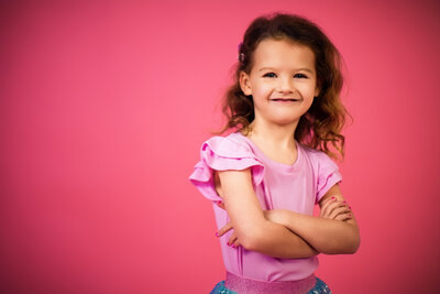 A brown headed girl poses with the sassy smirk on a solid pink backdrop with beautiful lighting in the senior photos pittsburgh studio.