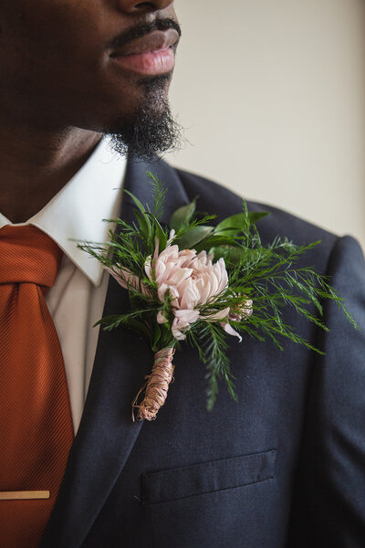 groom in a navy suit with a copper tie and pink floral boutonniere