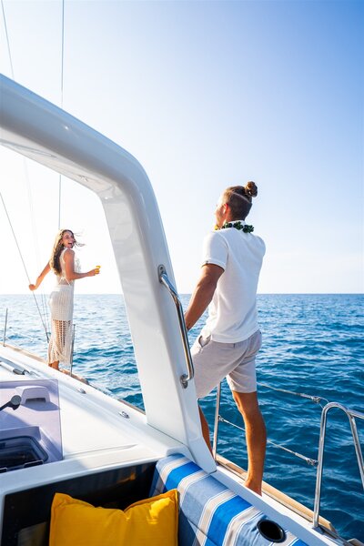 Couple enjoying their time on a Hawaii sailboat charter, smiling and taking in the ocean views as they stand on the deck together.