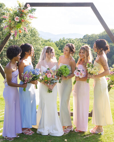 Bridesmaids and bride posing with their bouquets standing arm and arm in a row. Surrounded by lush greenery in the background.