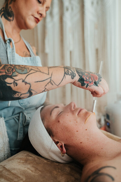 Libby uses a brush to apply a face mask to a client's face during their facial in her Eugene studio. 