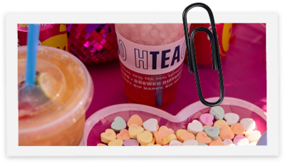 Sweet tarts in a heart bowl sitting on a pink table next to iced tea drinks.