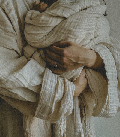 woman holding small child both wrapped up in cream colored cotton fabric