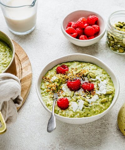 A vibrant matcha oats bowl topped with raspberries, coconut flakes, pumpkin seeds and bee pollen — a hormone-supportive, protein-rich breakfast for perimenopause.