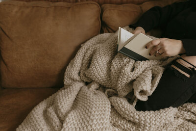Renee Hoffman reading a book on couch