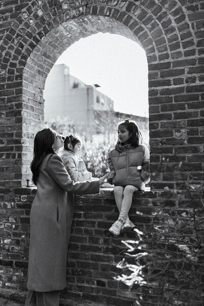 DUMBO brooklyn mom and 2 girls standing in archway with light shining on their faces