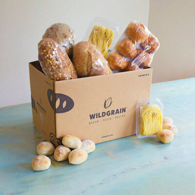 Sample box of Wildgrain delivery with breads and pastas coming out of the top and sitting on the sides. 