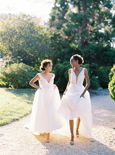 Softly lit portrait at Tudor Place of two brides walking hand-in-hand at an outdoor garden wedding, captured by a Fine Art Wedding Photographer Seattle.