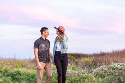 Couple hold hands while walking in a field of flowers on the California Coast.