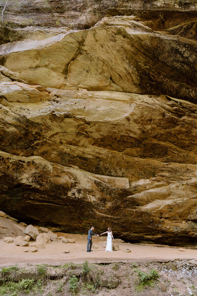 Groom walking towards bride with towering cliff behind them