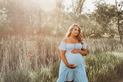 While the sun sets in the background, a momma cuddles into her baby bump during an outdoor maternity photoshoot near Bismarck, ND