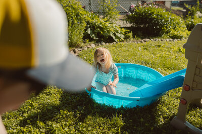 toddler girl laughs while sitting in a kiddie pool after sliding in on small slide