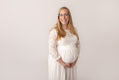 blonde pregnant woman wearing white lace dress in studio by philadelphia maternity photographer