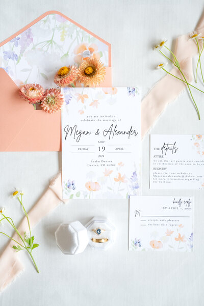 Wedding flat lay photo of wedding invitation suites, florals, ribbon, and rings