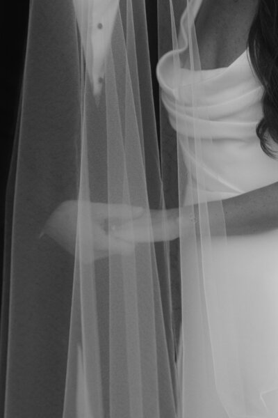 A close-up shot of the couple holding hands beneath the bride’s veil