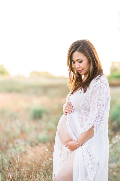 Pregnant woman with white dress exposing her pregnant belly and standing in an open field