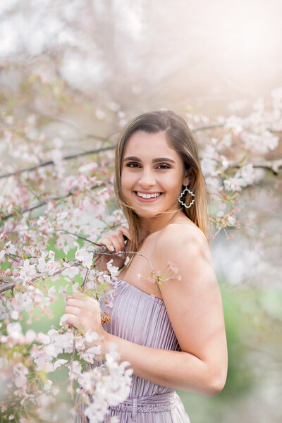 Natural and pretty senior picture of a girl surrounded by Cherry blossoms wearing a lavender dress