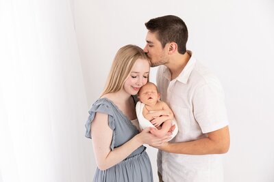 Dad kissing mom's forehead while she holds new baby by Maryland Newborn Photographer