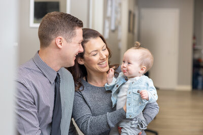 Husband and wife small business owners holding their baby girl in the chiropractic office.