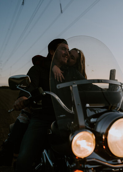 Couple kissing on back of motorcycle.