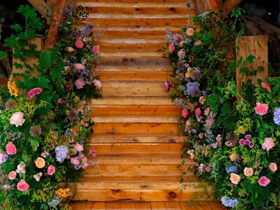Wooden stairs lined with vibrant, seasonal floral arrangements in jewel tones including purple, red, and coral, surrounded by lush greenery.