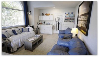 Living room with kitchenette, and blue couch. Bathrobes hanging on the door