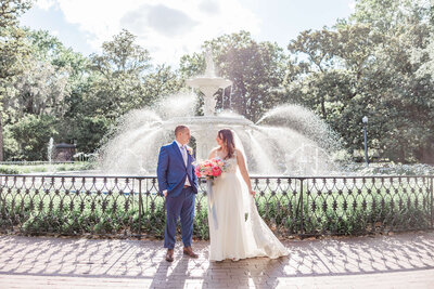 Bride and groom standing in front of the Forsyth Park fountain in Savannah, GA, holding a vibrant bouquet during their elopement.