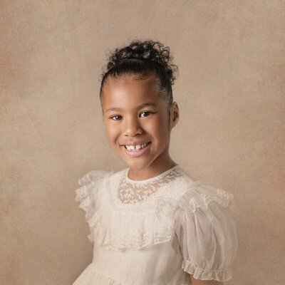 Smiling girl in white dress photographed through children’s photography in Michigan