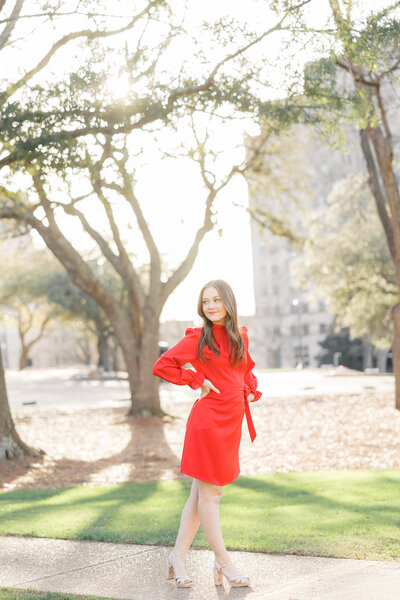 teenage girl in a red dress standing in front of trees and buildings
