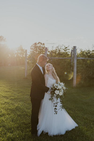 photo of bride and groom standing in a vineyard smiling and looking at each other taken by Stoughton wedding photographer