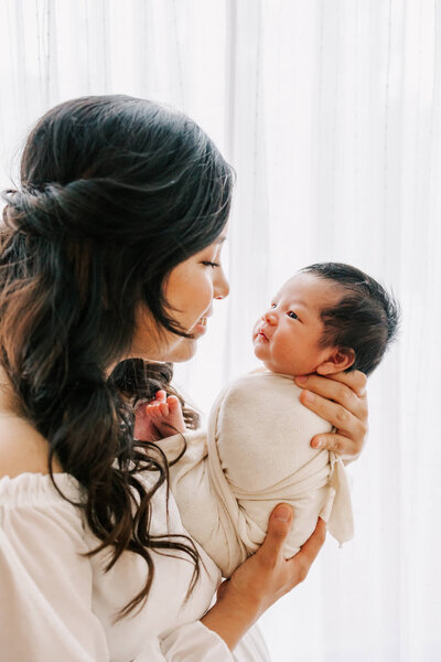sweet portrait of mom with black hair looking at infant boy who is looking back at her